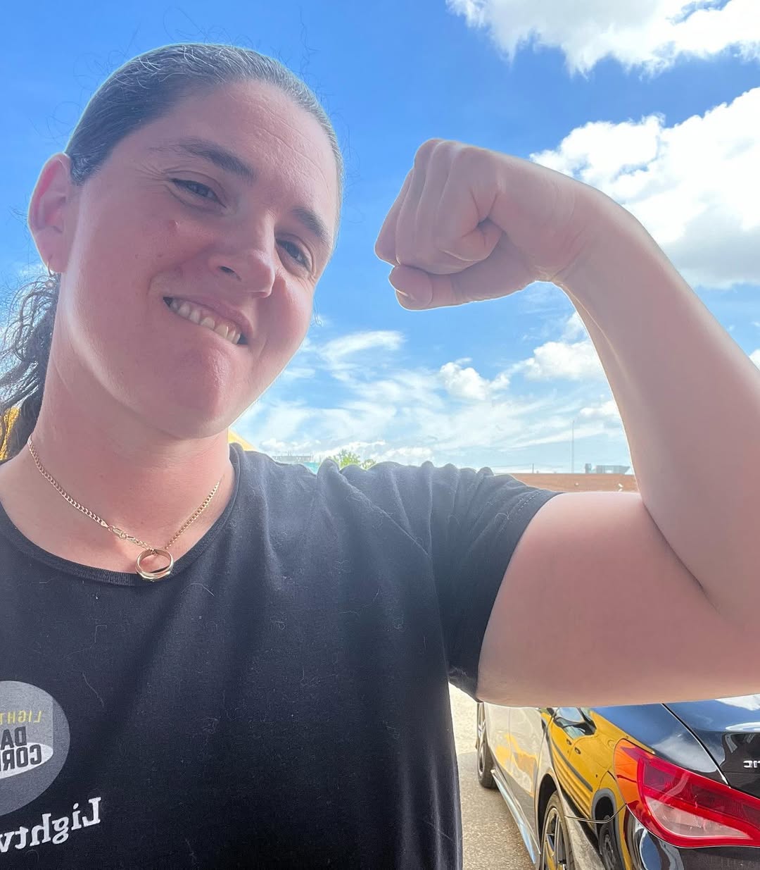 Sarah smiling and flexing her arm beneath a blue sky